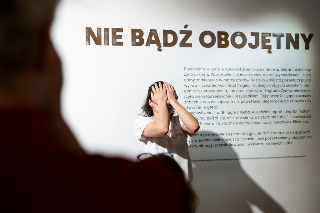 Visitor viewing Polish language exhibit panel reading NIE BADZ OBOJETNY.