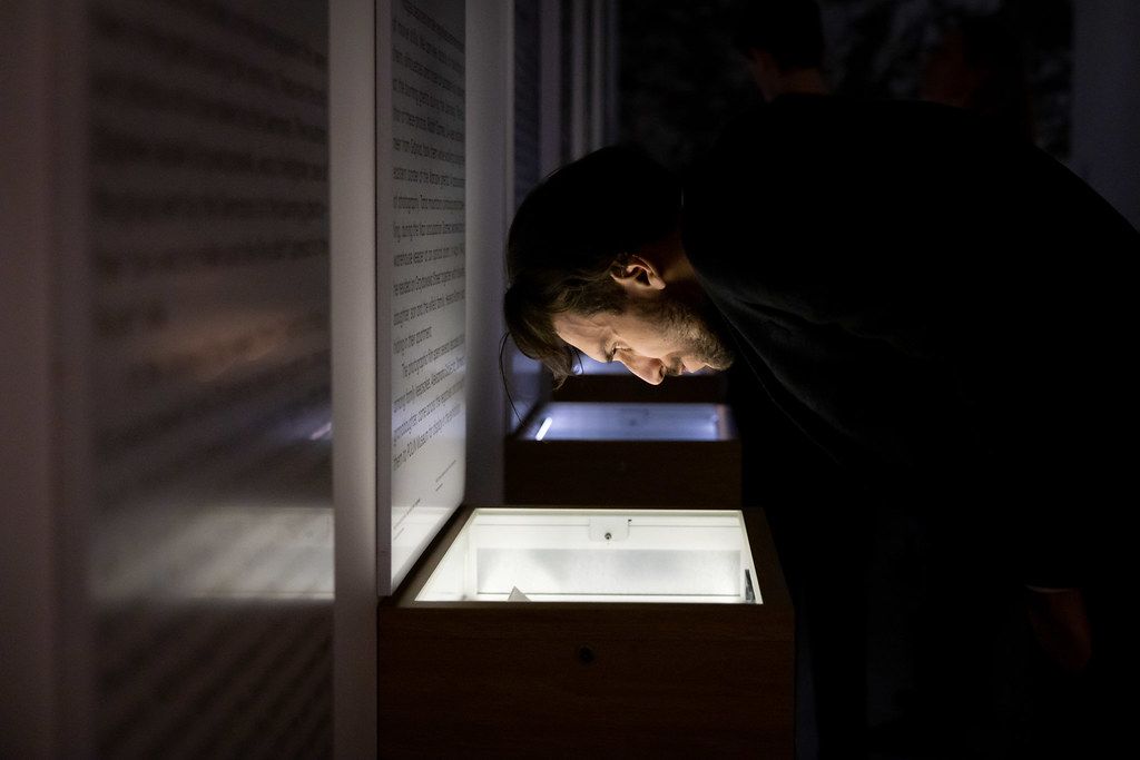 Person examining illuminated display box in dark room.