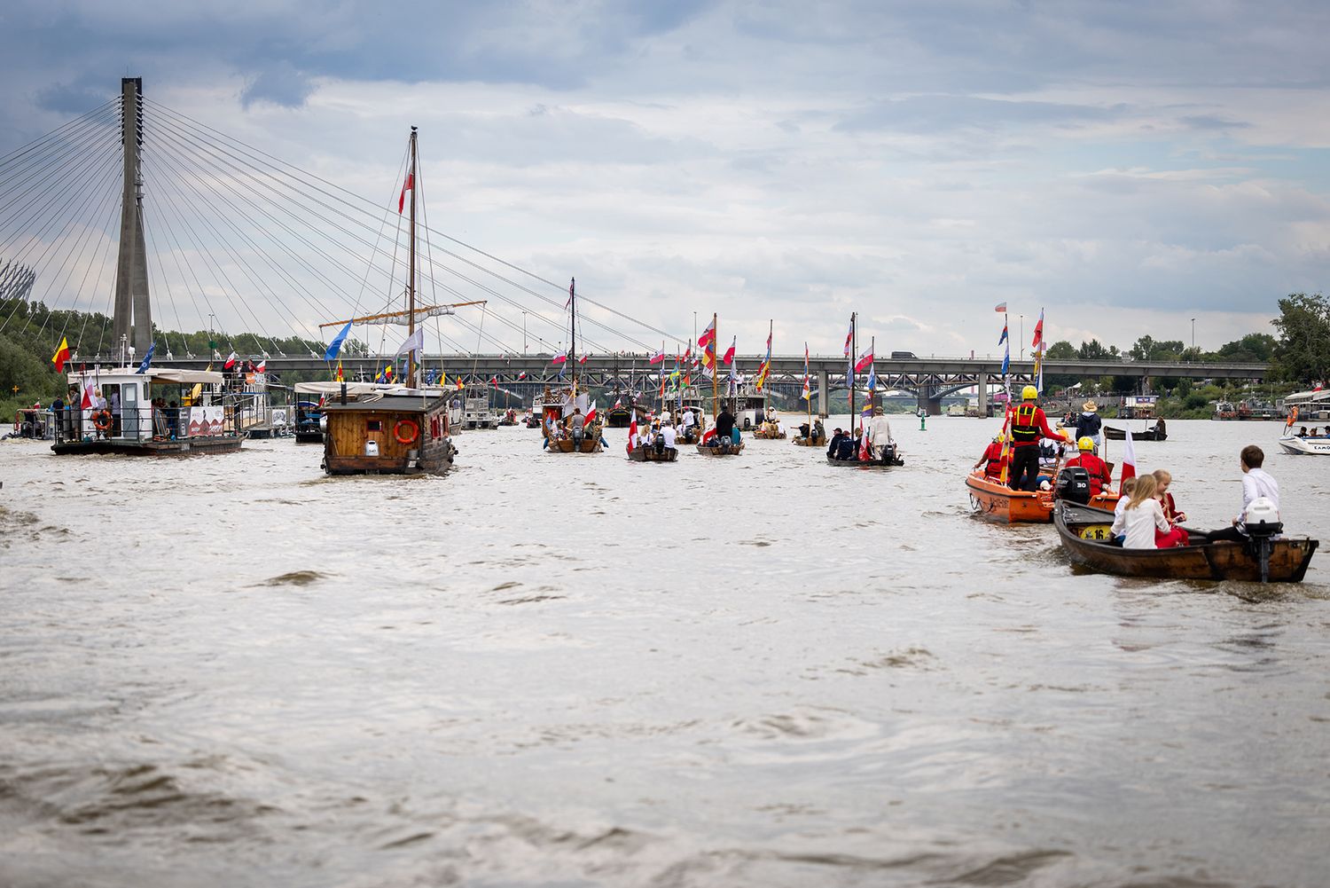 Colorful flotilla of boats on river with cable-stayed bridge in background during festival.