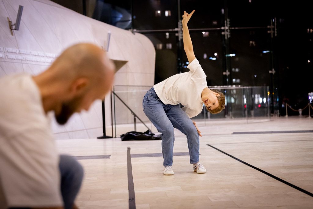 Two dancers perform expressive contemporary dance moves in a modern architectural space.