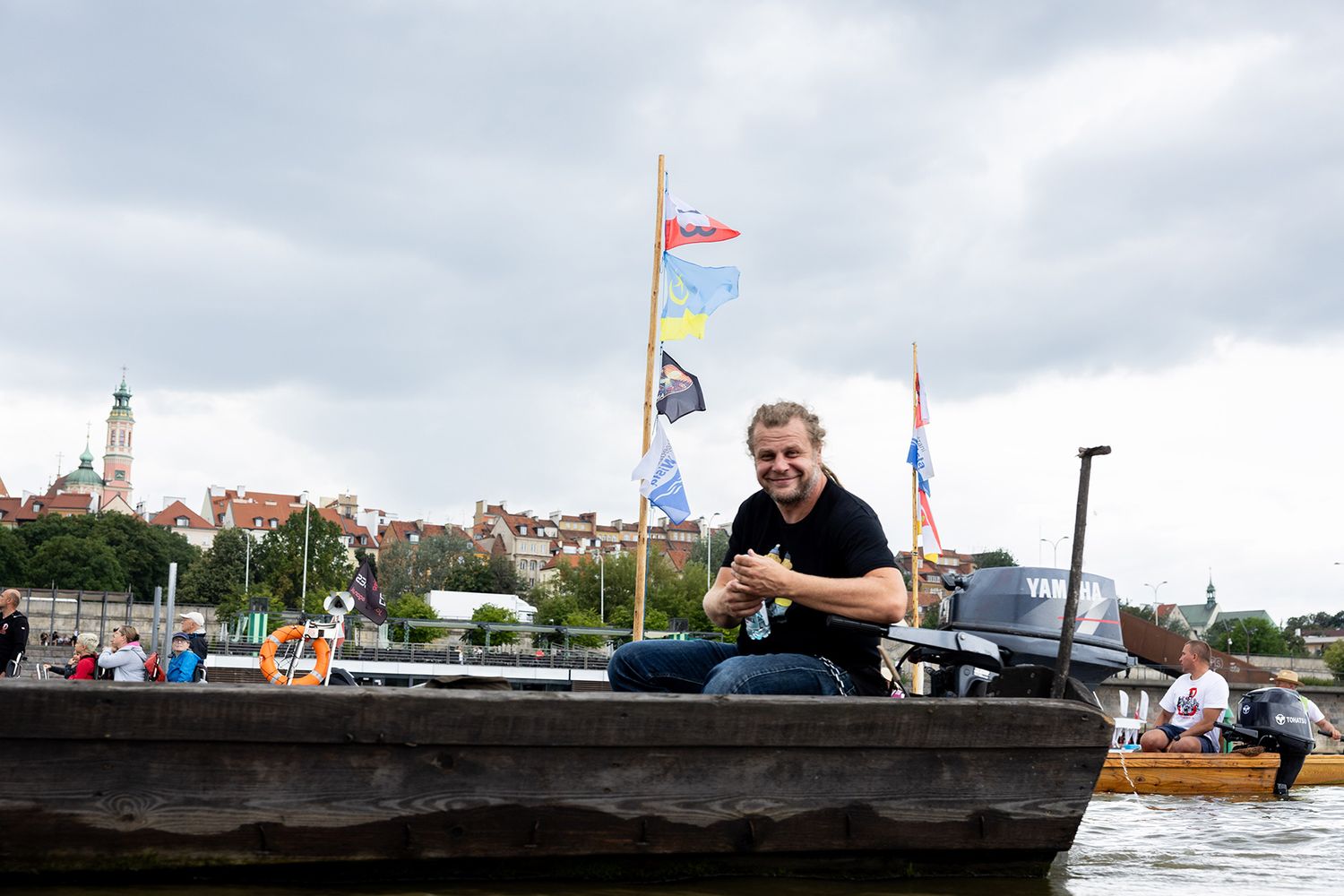 Smiling man sitting in wooden boat on river with colorful flags during water festival.
