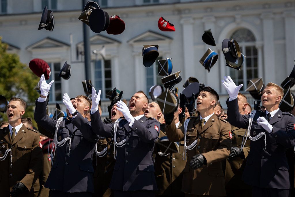Military graduates tossing caps in celebration outside historic building.