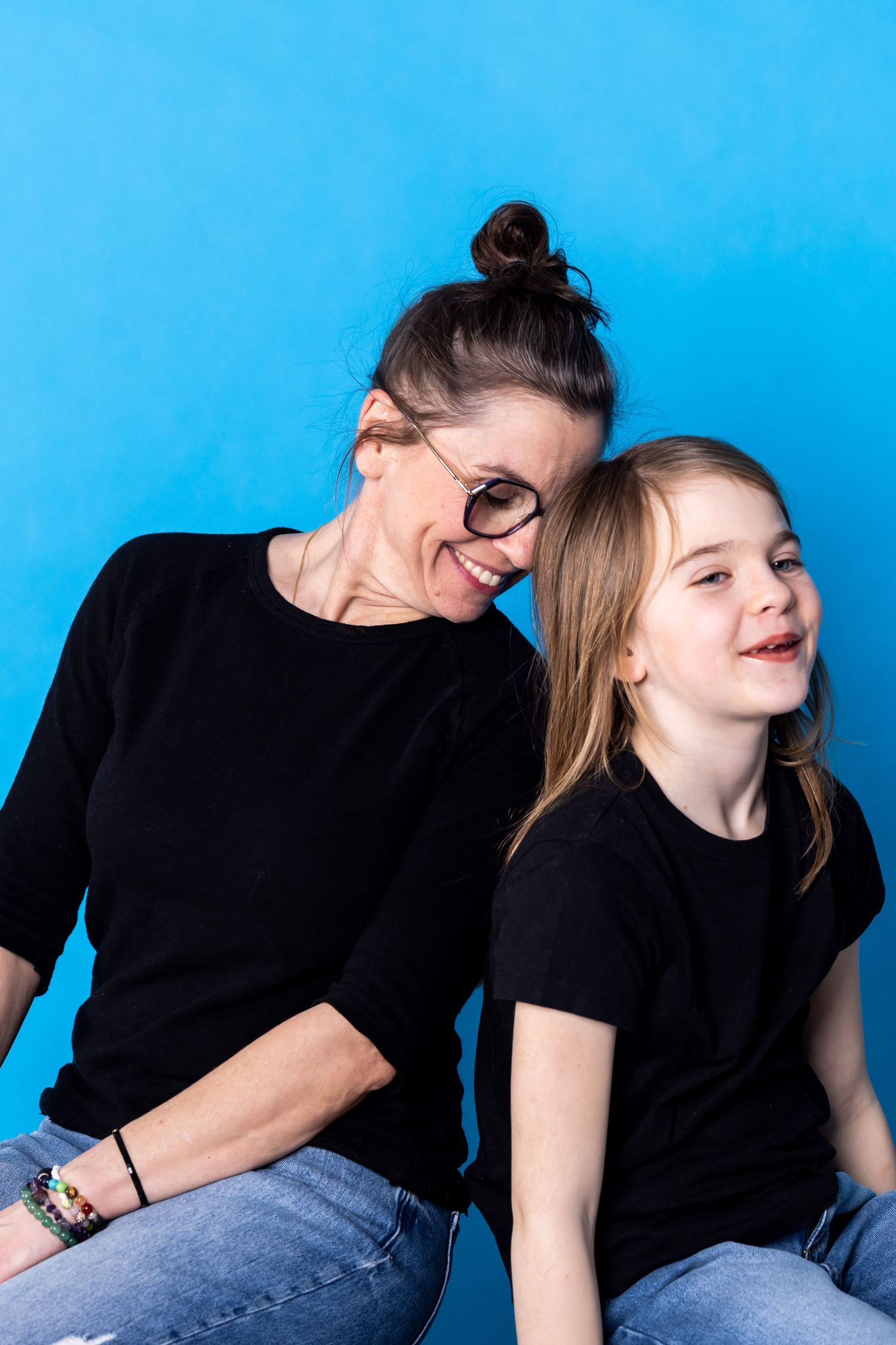 Smiling woman and young girl in matching black shirts on blue background.