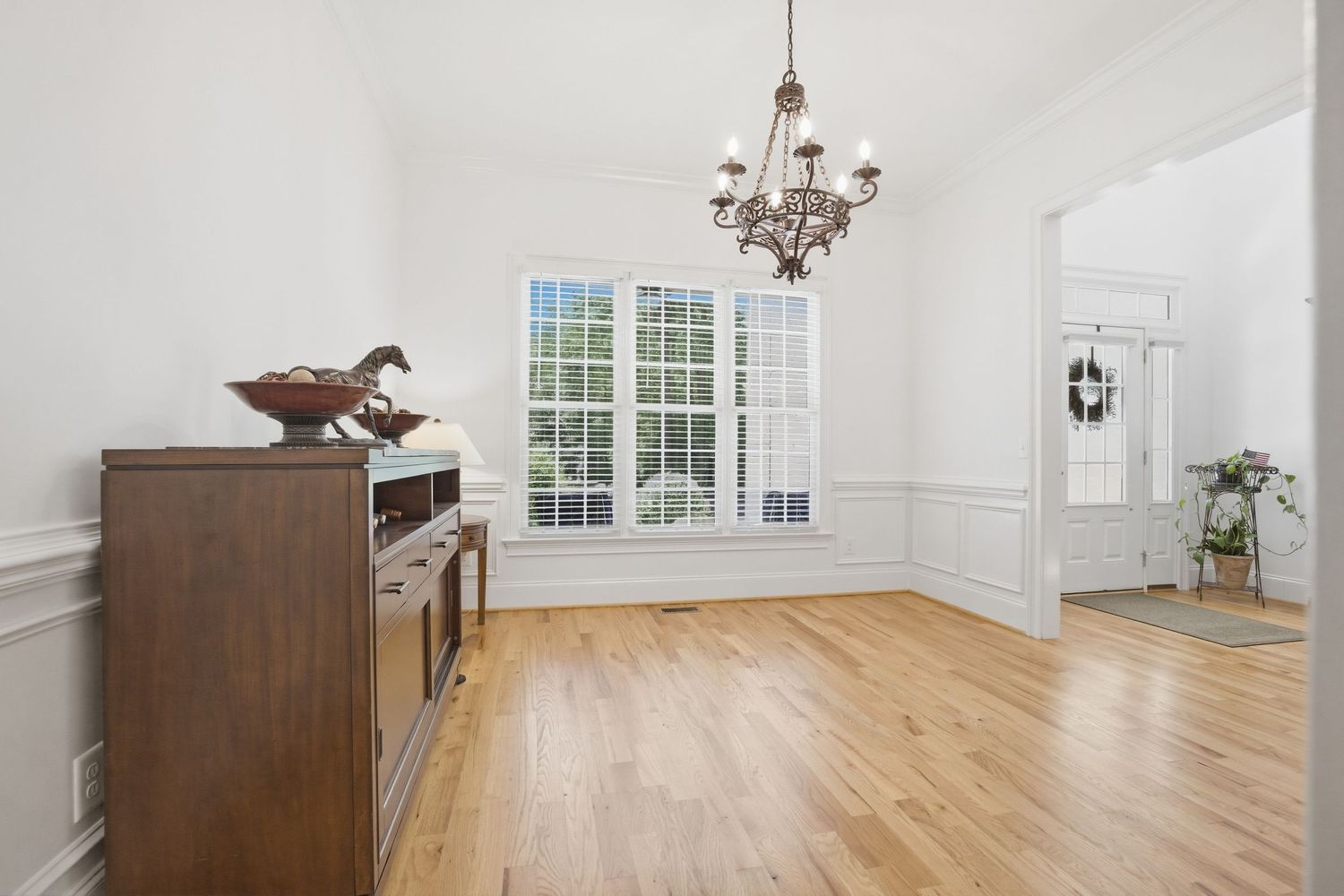 Formal dining room with wainscoting, chandelier, hardwood floors, and French doors with natural light.