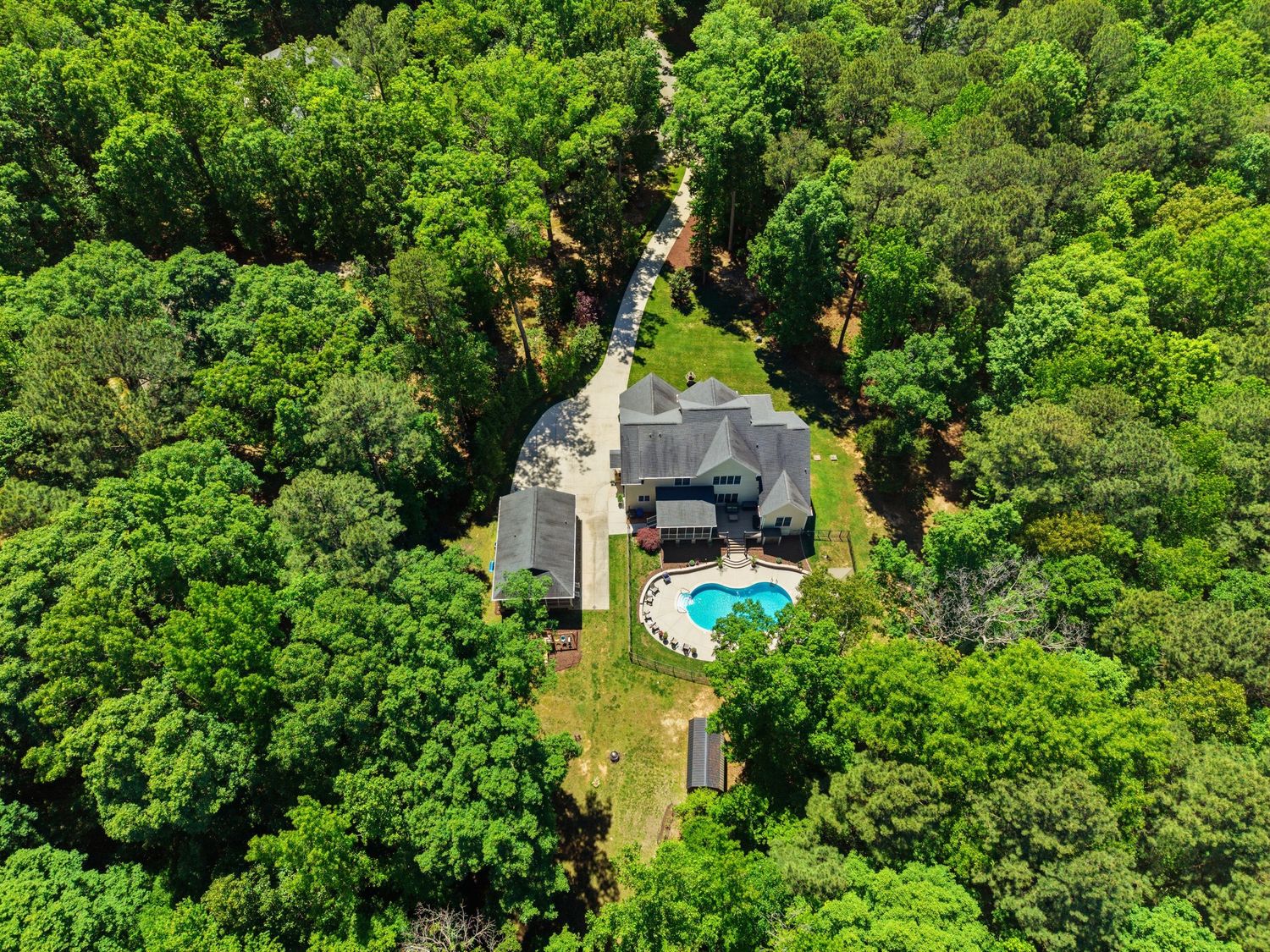 Drone view of secluded luxury home with swimming pool nestled within dense forest surroundings.