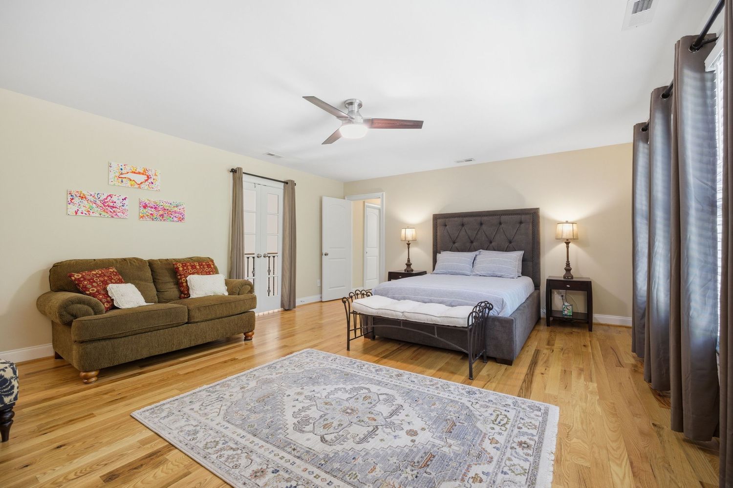 Spacious master bedroom with hardwood floors, tufted headboard, ceiling fan, and elegant area rug.