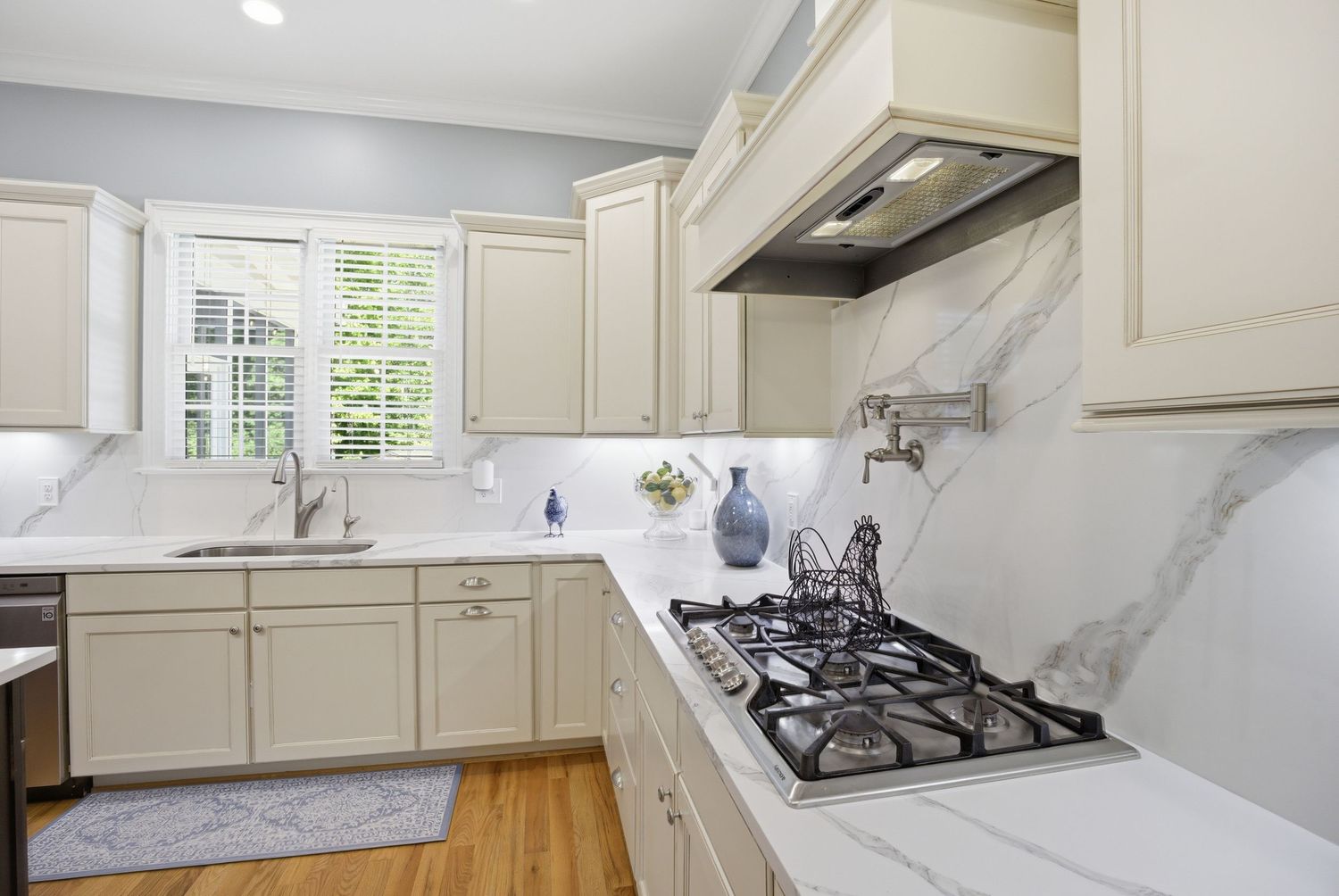 Bright kitchen with cream cabinets, marble backsplash, gas cooktop, pot filler, and white quartz countertops.
