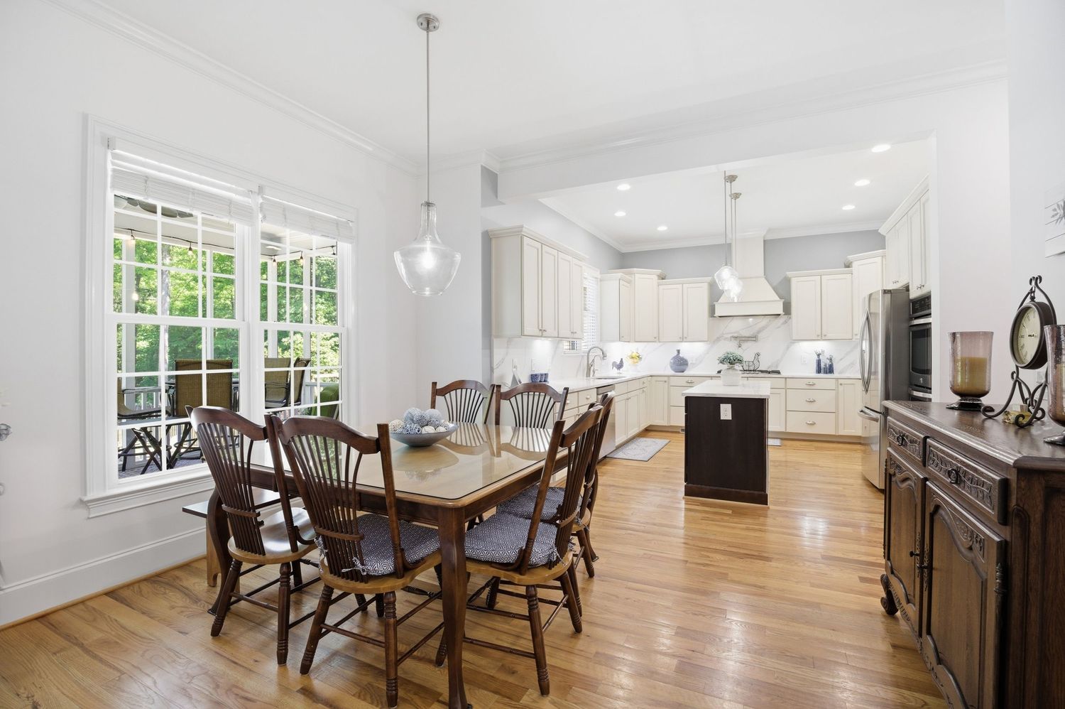 Dining area with wood table, pendant lights, and view into white kitchen with island and stainless steel appliances.