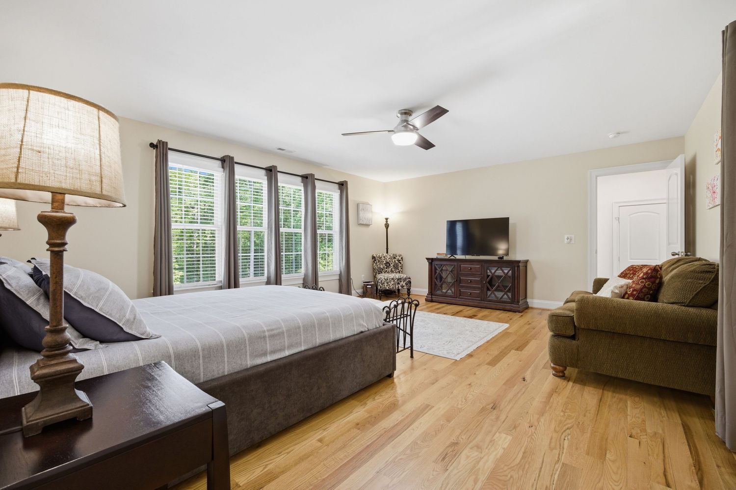 Bright master bedroom featuring hardwood floors, large windows, ceiling fan, and sitting area.
