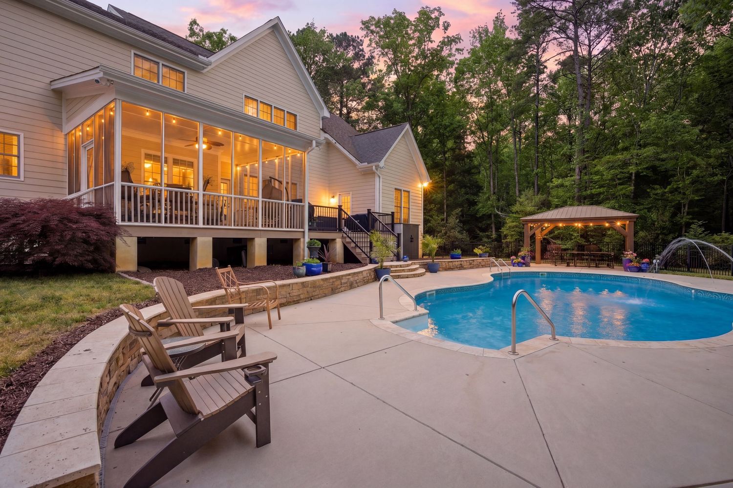 Virtual Twilight backyard view featuring illuminated screened porch, swimming pool with fountain, and gazebo amid trees.