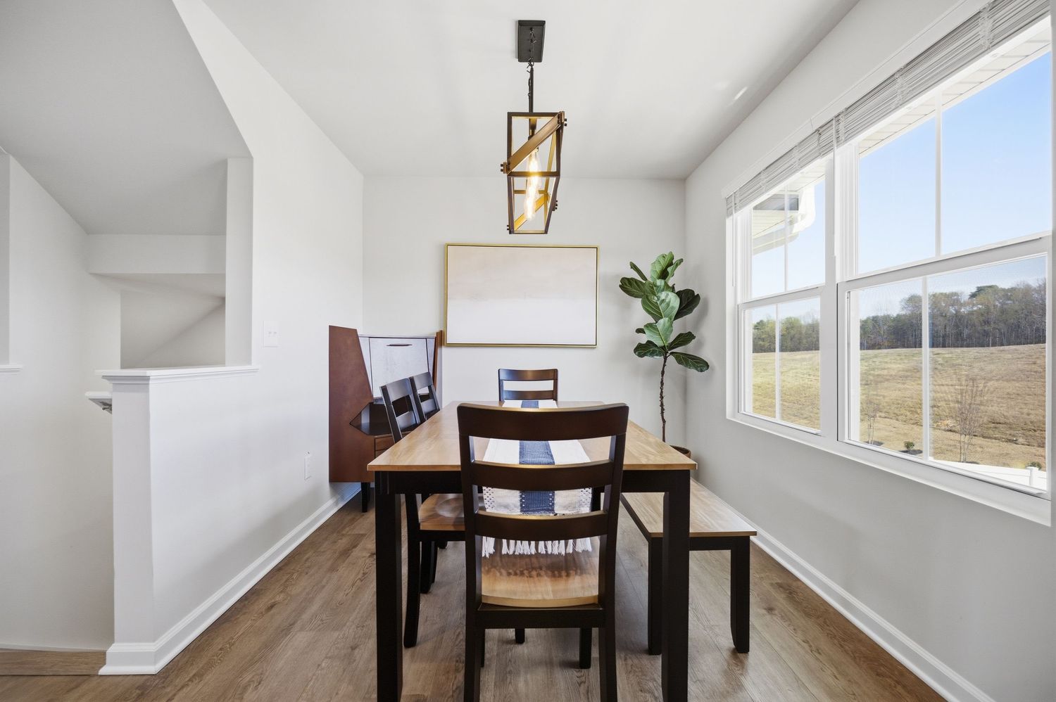 Cozy dining area with wooden table, dark chairs, geometric pendant light, and large window with field view.
