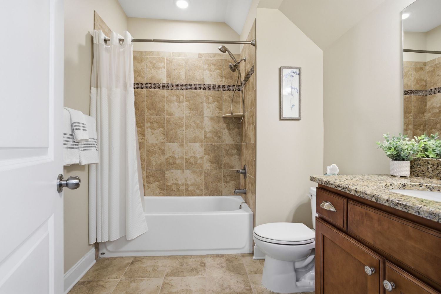 Full bathroom with tiled shower-tub combo, white curtain, toilet, wood vanity, and granite countertop.