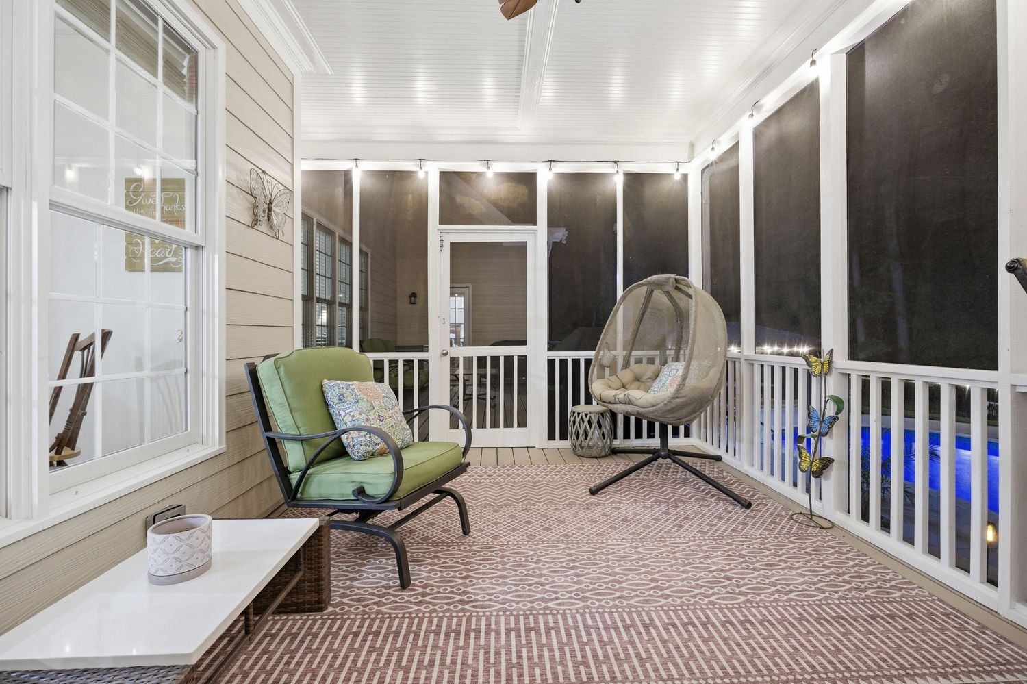 Cozy screened porch at night featuring hanging chair, green cushioned seating, and pool view.