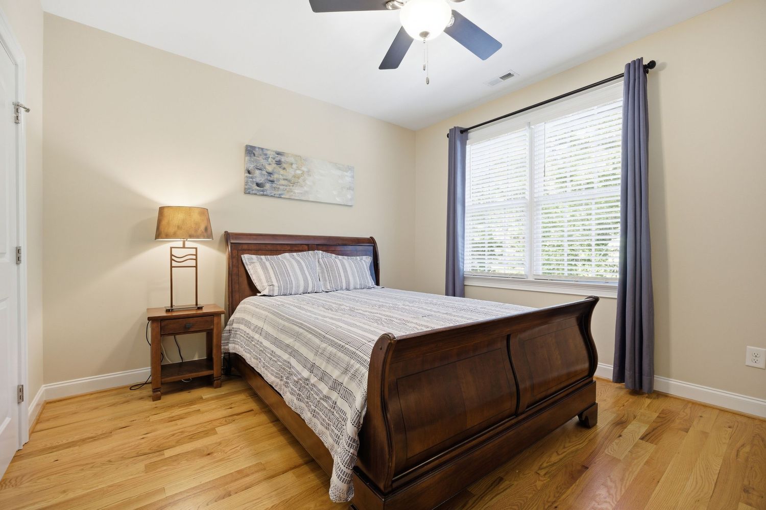 Bedroom featuring dark wood sleigh bed, hardwood floors, ceiling fan, and bright window with blinds.