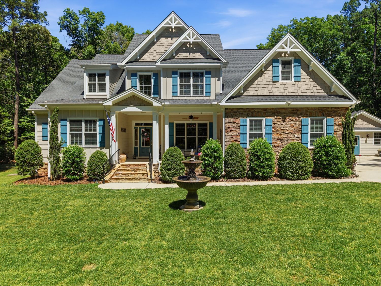 Beautiful craftsman home featuring blue shutters, stone accents, decorative gables, and lush landscaping.