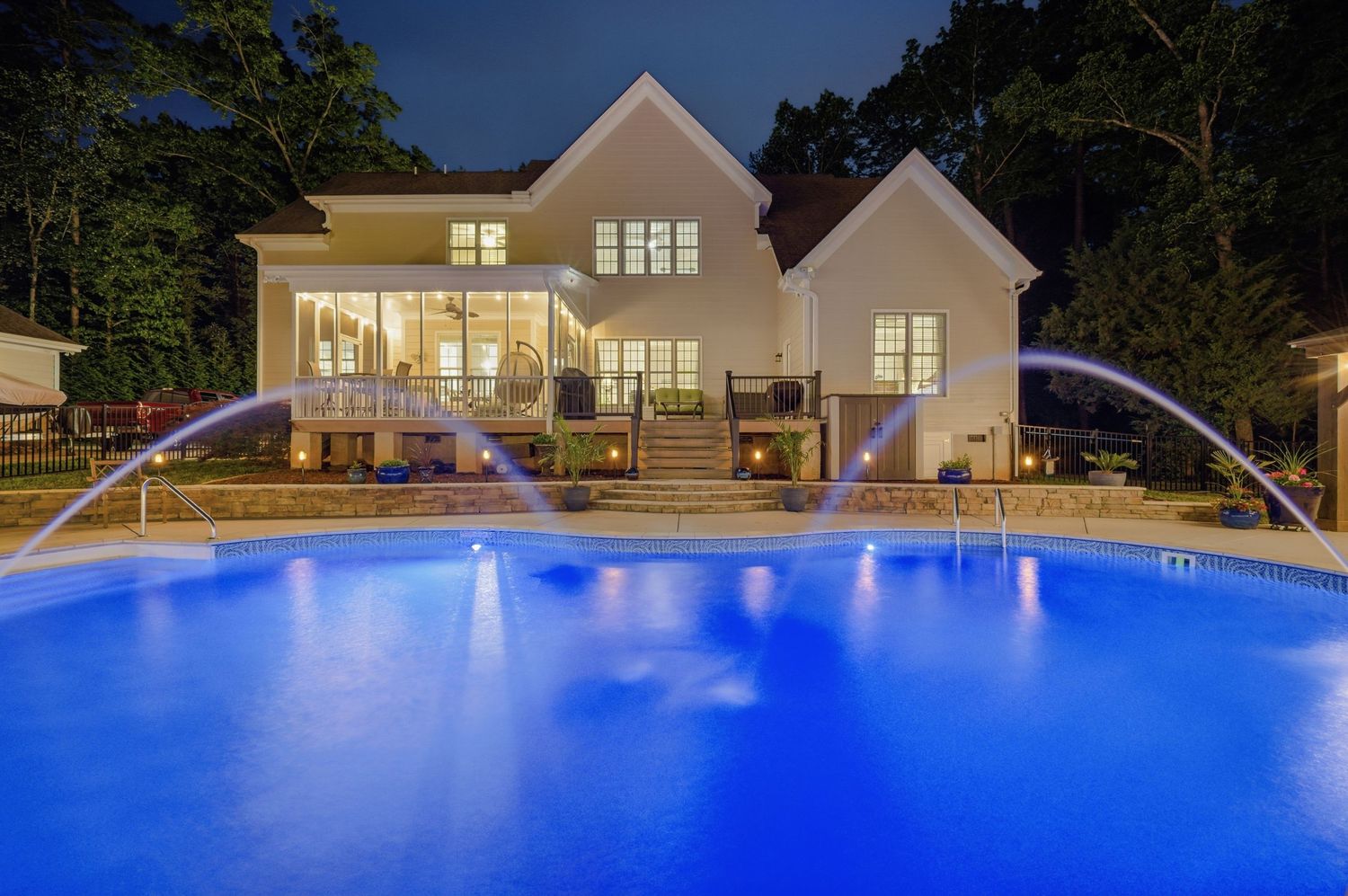 Stunning backyard pool with water features illuminated at night with elegant home backdrop.