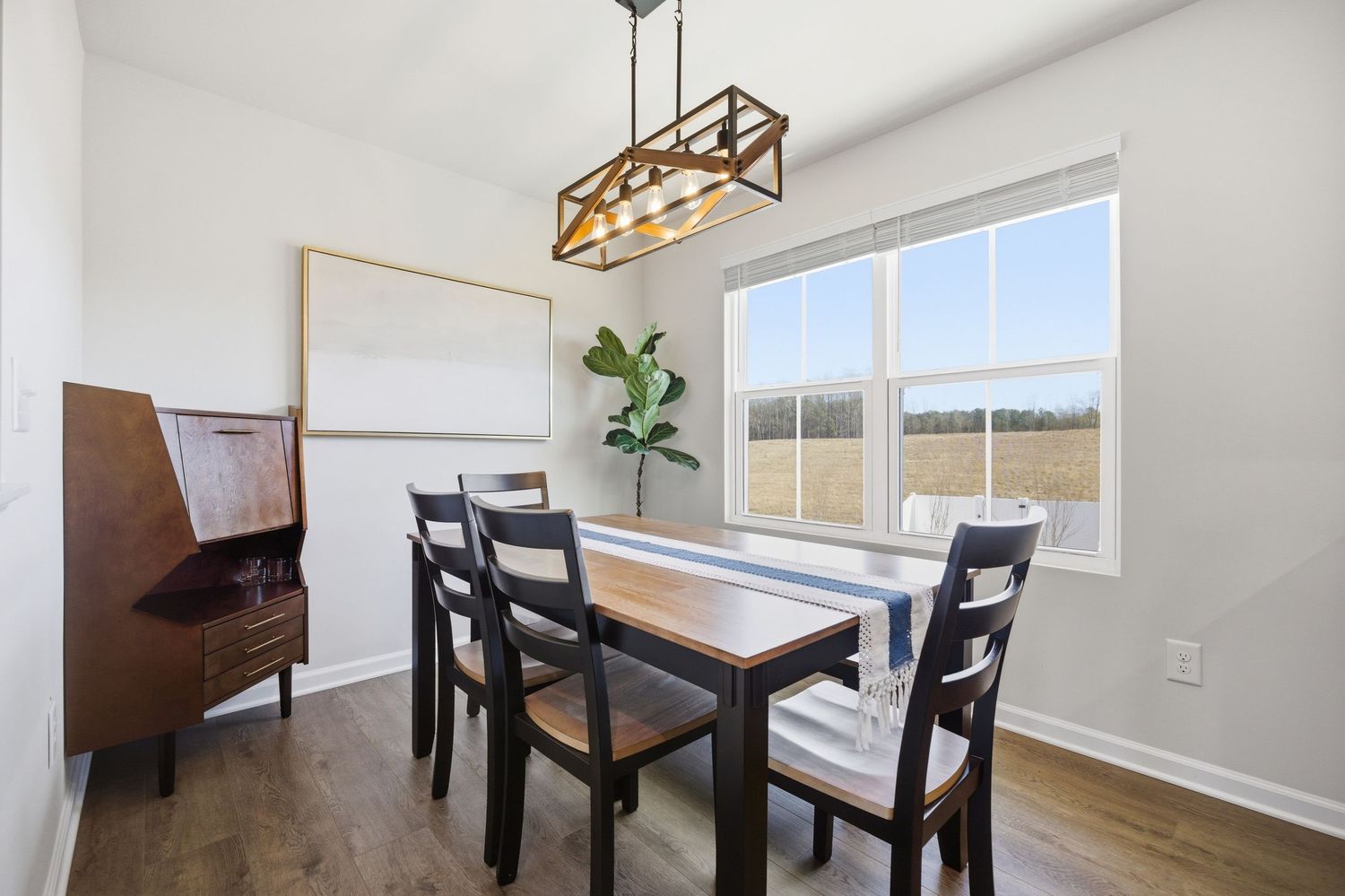 Cozy dining area with wood table, dark chairs, geometric chandelier, and bright window view.