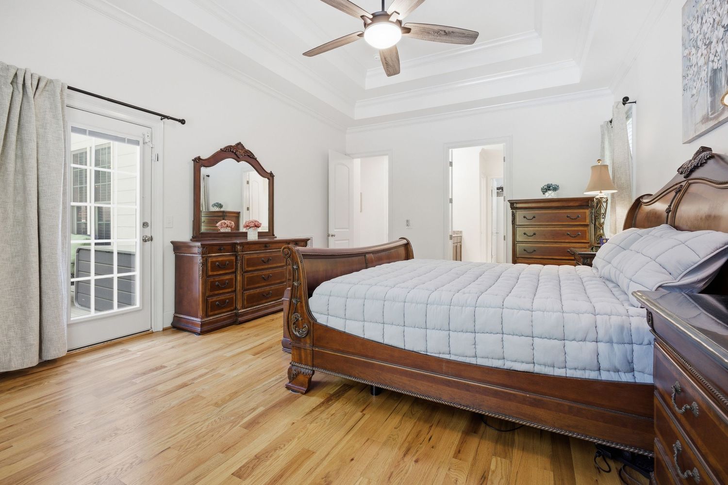 Elegant master bedroom featuring dark wood furniture, tray ceiling, hardwood floors, and French door access.