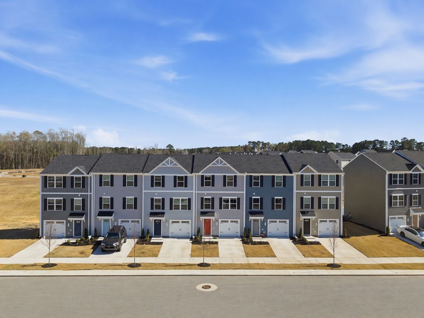 Row of two-story townhomes with gray siding, white shutters, and attached garages on quiet street.