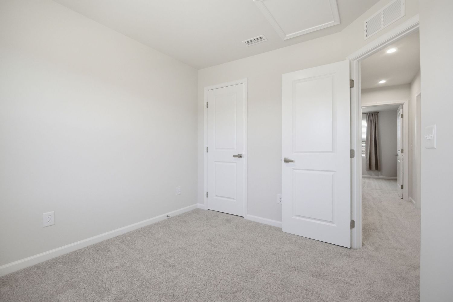 Bright empty bedroom with light gray carpet, white walls, two white doors, and neutral finishes.
