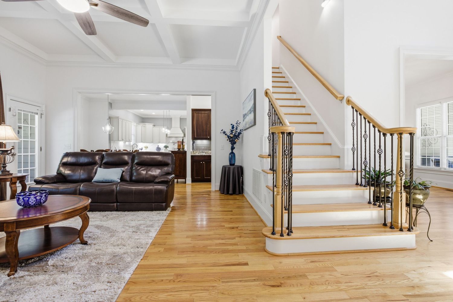 Grand foyer with hardwood floors, coffered ceiling, elegant staircase with iron balusters, and formal living area.