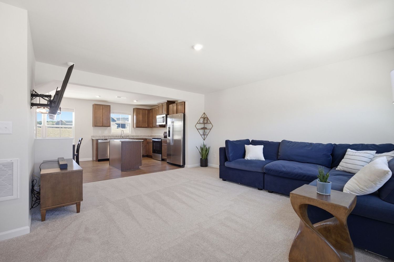 Open concept living room with blue sofa and view into kitchen with stainless appliances.