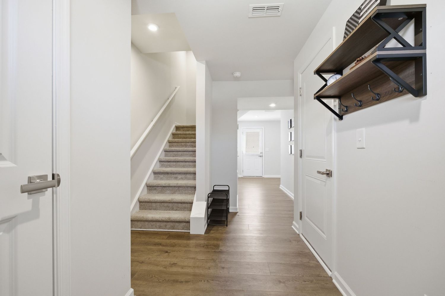 Bright entryway with white walls, hardwood floors, staircase, and decorative wall-mounted coat rack.