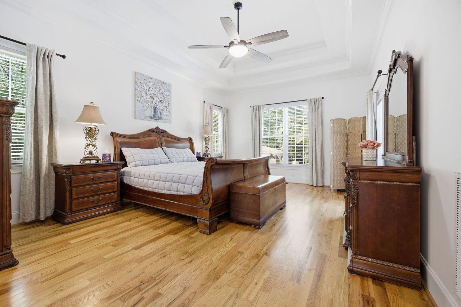 Spacious master bedroom with hardwood floors, tray ceiling, ceiling fan, and French doors to outdoor space.