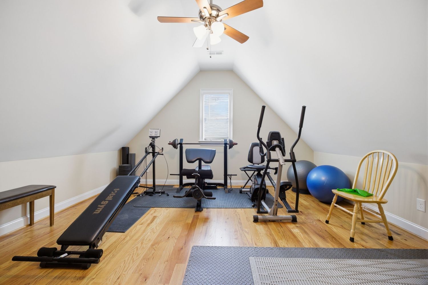Attic home gym with sloped ceilings, workout equipment, hardwood floors, and ceiling fan.