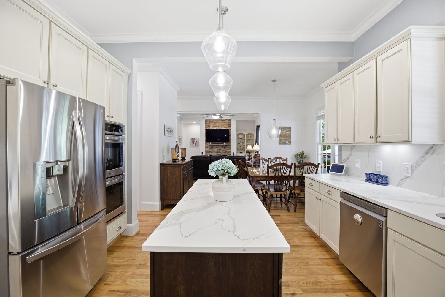 Large kitchen island with white quartz top, cream cabinets, stainless appliances, and hardwood floors.