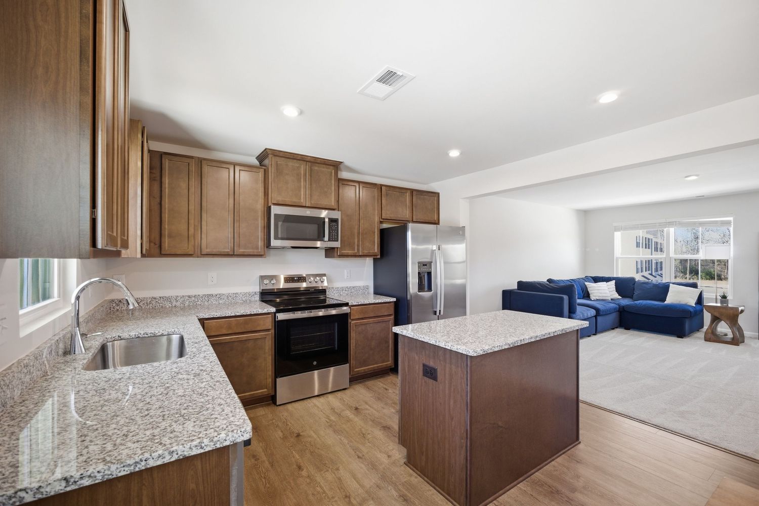Open kitchen with brown cabinets, granite counters, stainless appliances, and adjacent living room.
