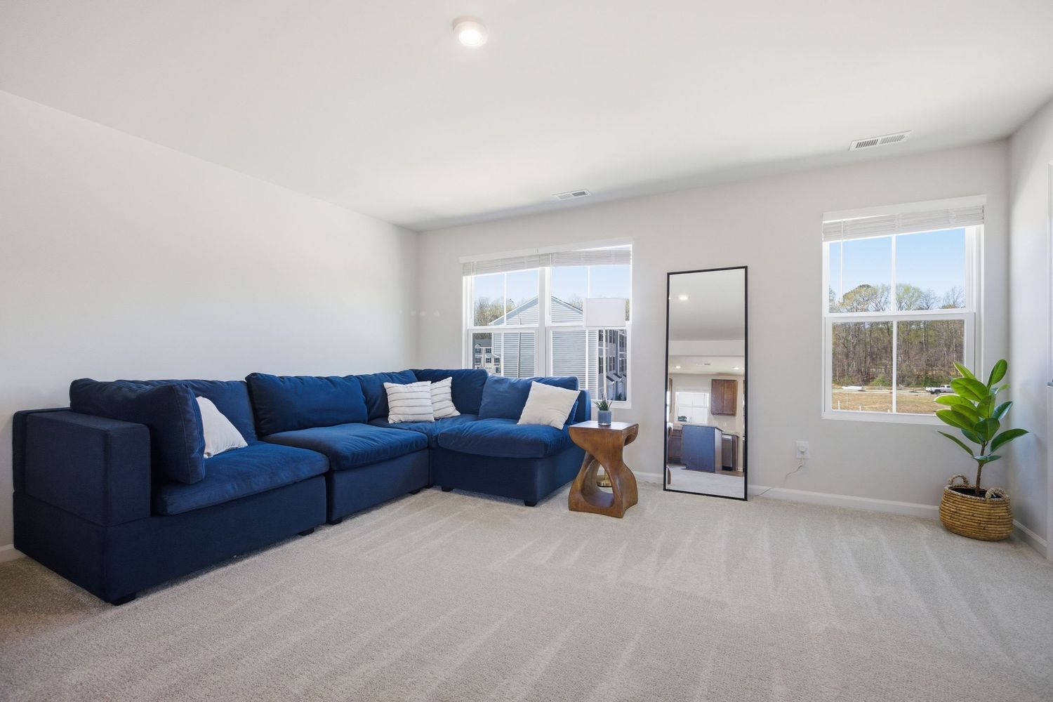 Spacious living room with blue sectional sofa, large windows, and neutral carpet flooring.