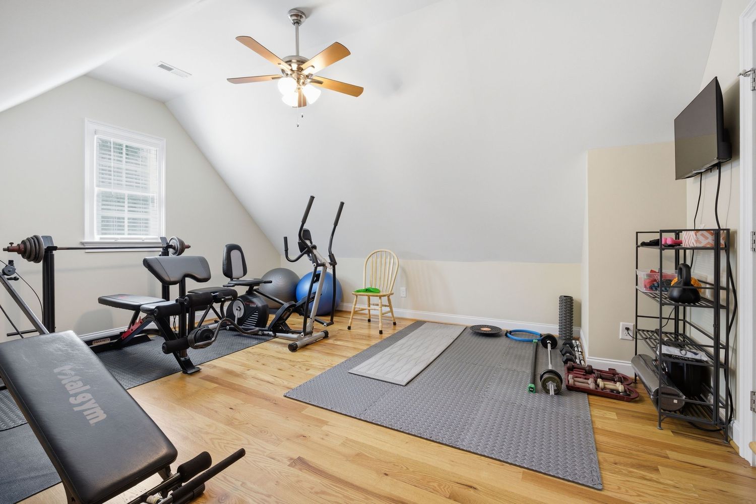 Vaulted ceiling home gym with exercise equipment, hardwood floors, ceiling fan, and wall-mounted TV.