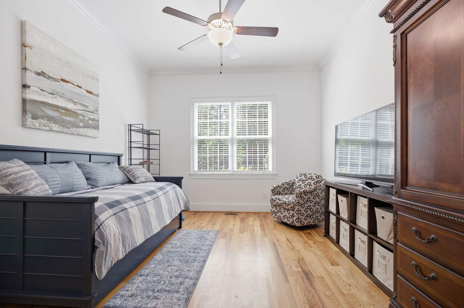 Bedroom with navy blue bed frame, hardwood floors, ceiling fan, and large window with natural light.