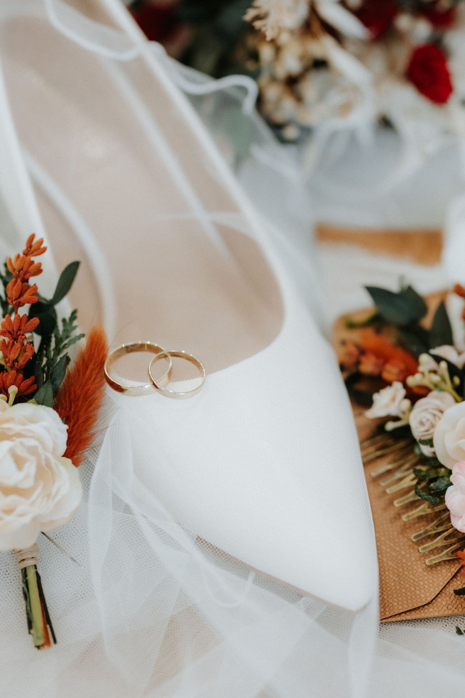 White bridal heels with gold wedding rings, floral boutonniere, and hair comb on a delicate veil.