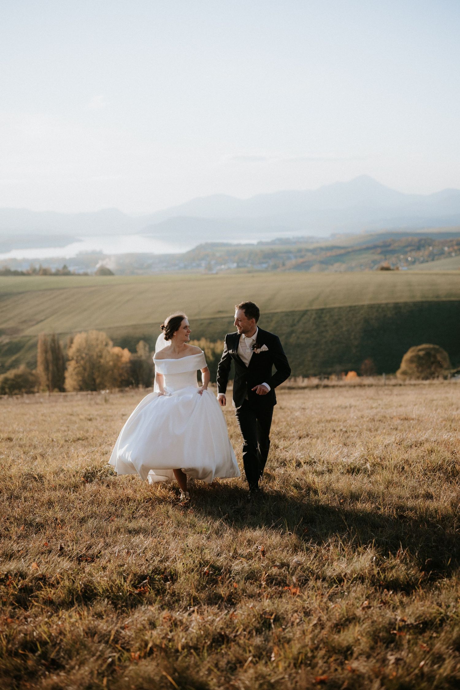 Bride and groom running through golden autumn fields with misty mountains in the background on their wedding day.