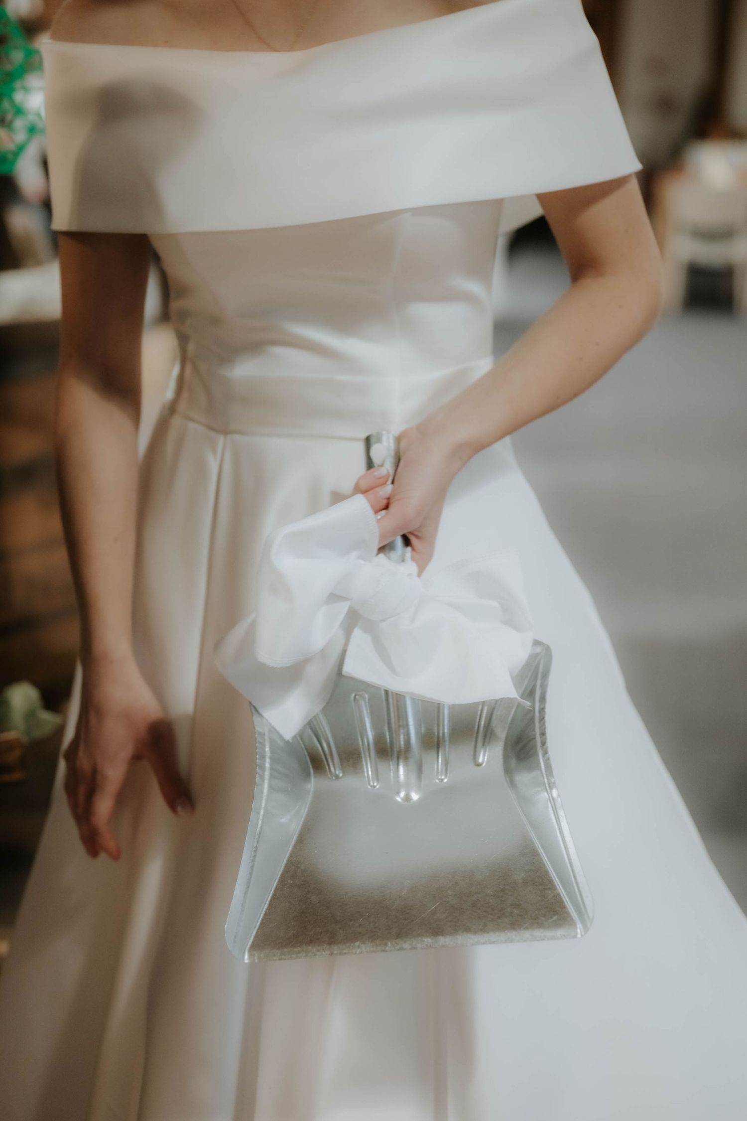 Bride in off-shoulder white gown holding elegant clear acrylic clutch bag with white bow detail.