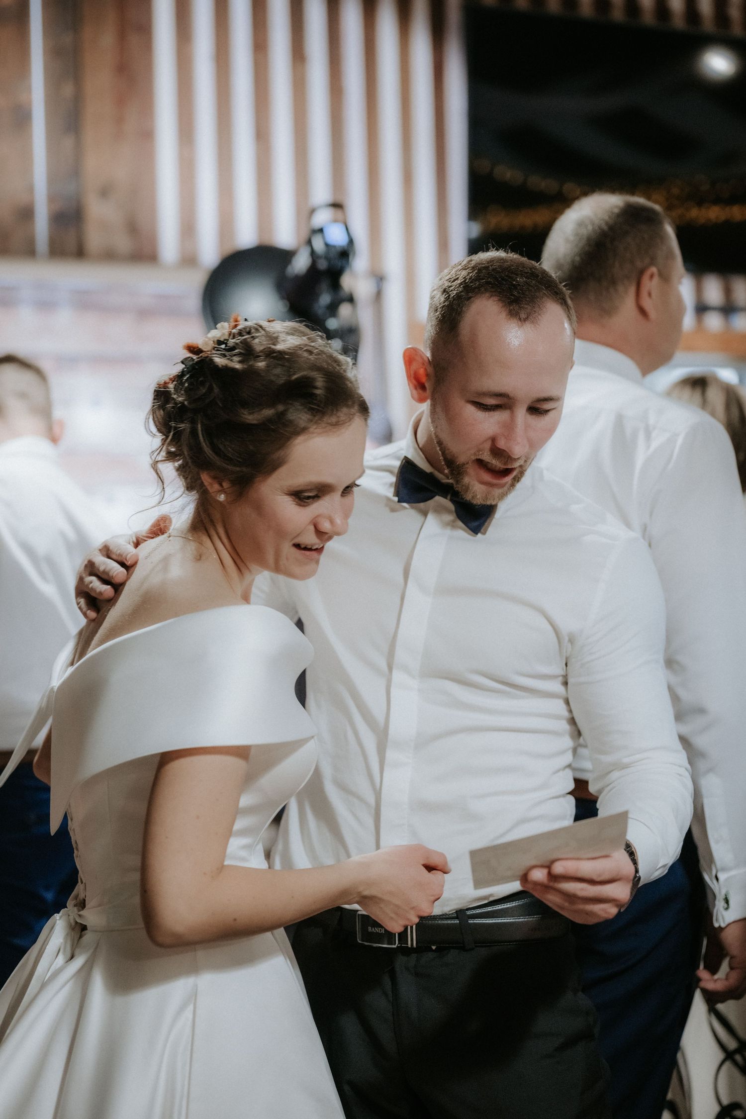 Bride and groom reading a card together at their wedding reception, dressed in white wedding attire.