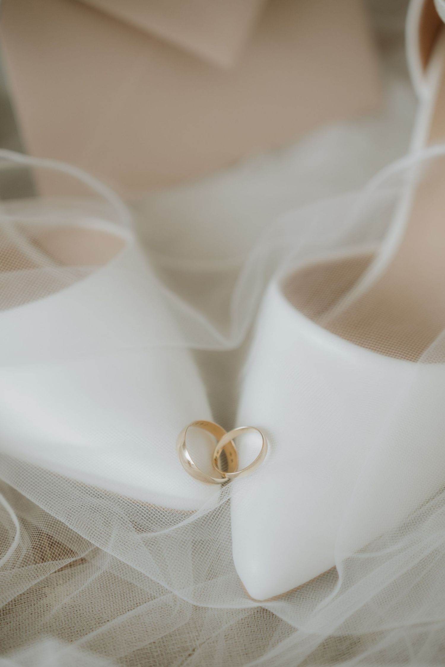 Two gold wedding rings resting on white bridal heels surrounded by delicate tulle veil fabric.