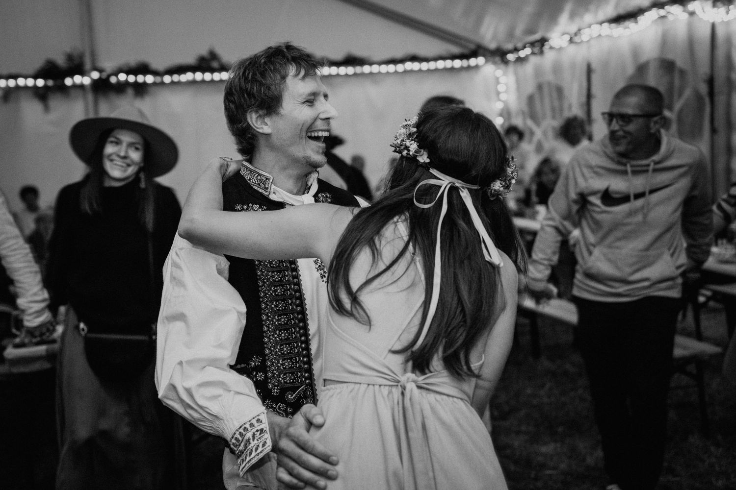 Black and white photo of a joyful couple dancing and embracing at a wedding reception under a tent.