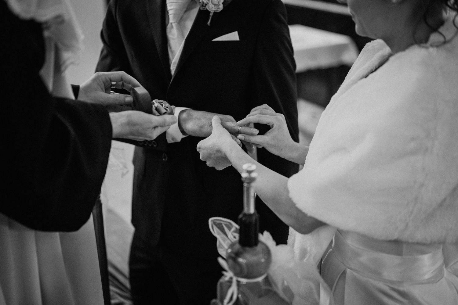 Black and white wedding ring exchange ceremony photo with bride and groom hands.