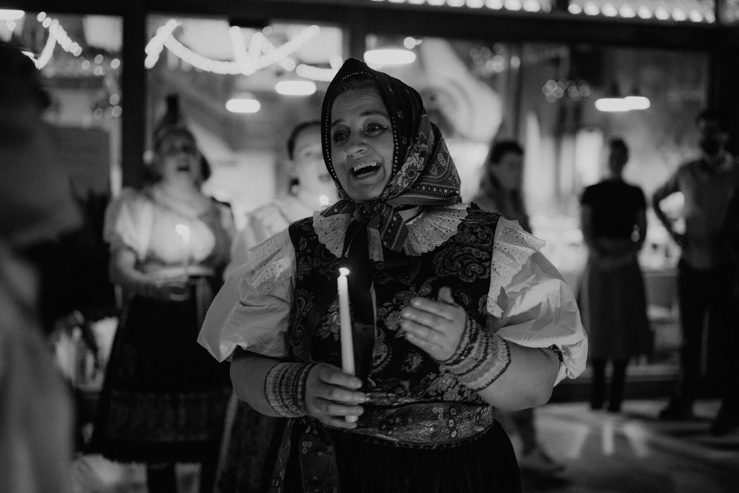 Elderly woman in traditional folk costume holding a candle, black and white photography.