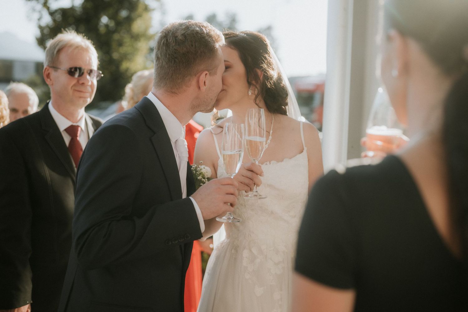 Bride and groom sharing a kiss while holding champagne glasses at their wedding reception outdoors.