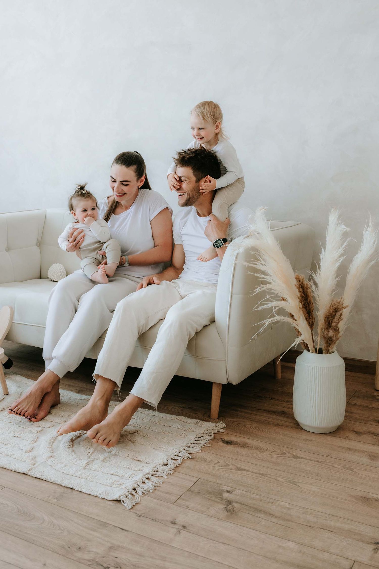 Happy family of four relaxing together on a white sofa in a bright living room.