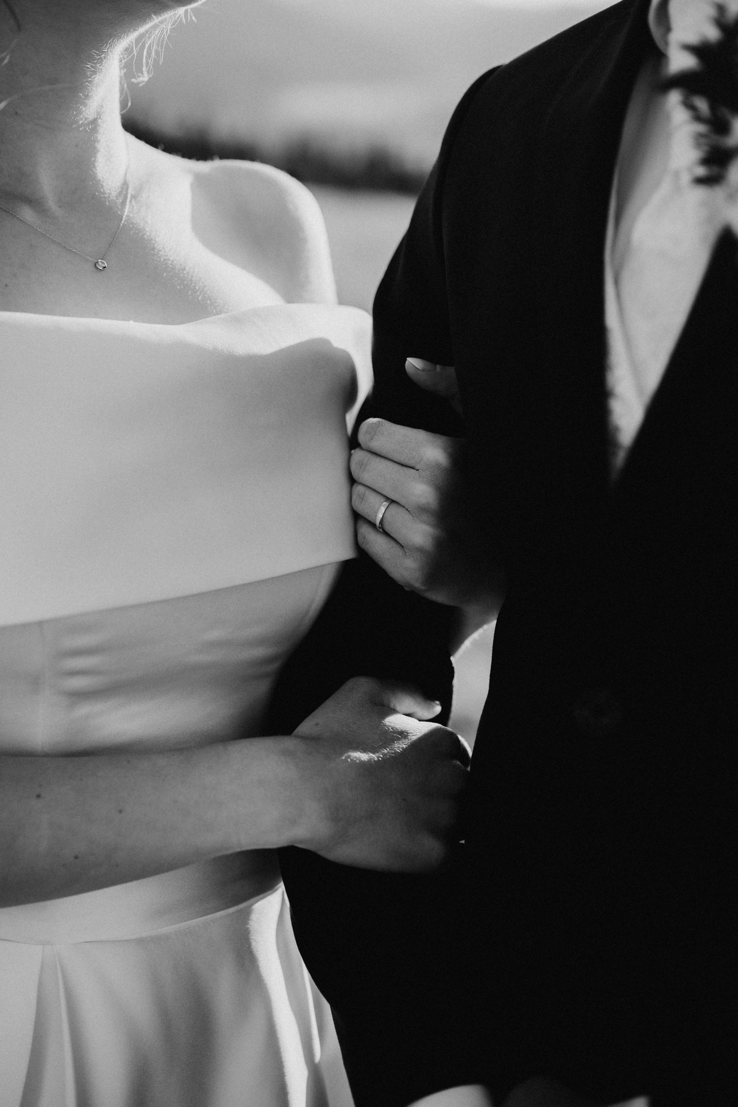 Black and white photo of a bride and groom embracing, showing wedding ring on bride's hand.