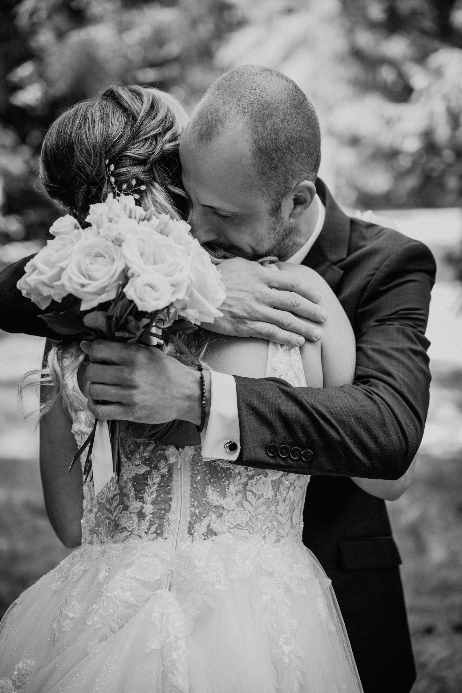 Black and white photo of groom embracing bride holding rose bouquet at wedding ceremony.