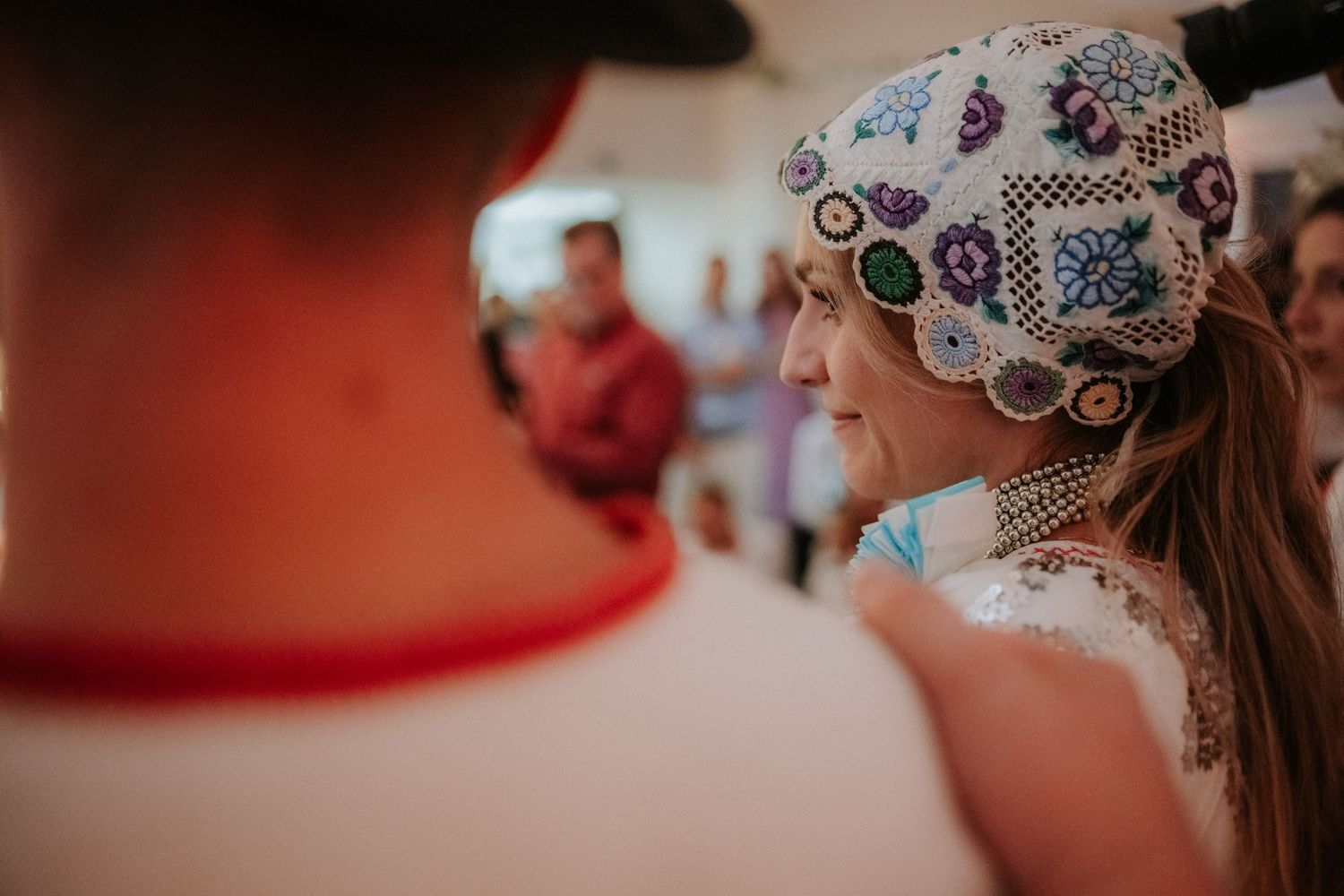 Woman wearing ornate beaded folk headdress smiling at traditional cultural event.