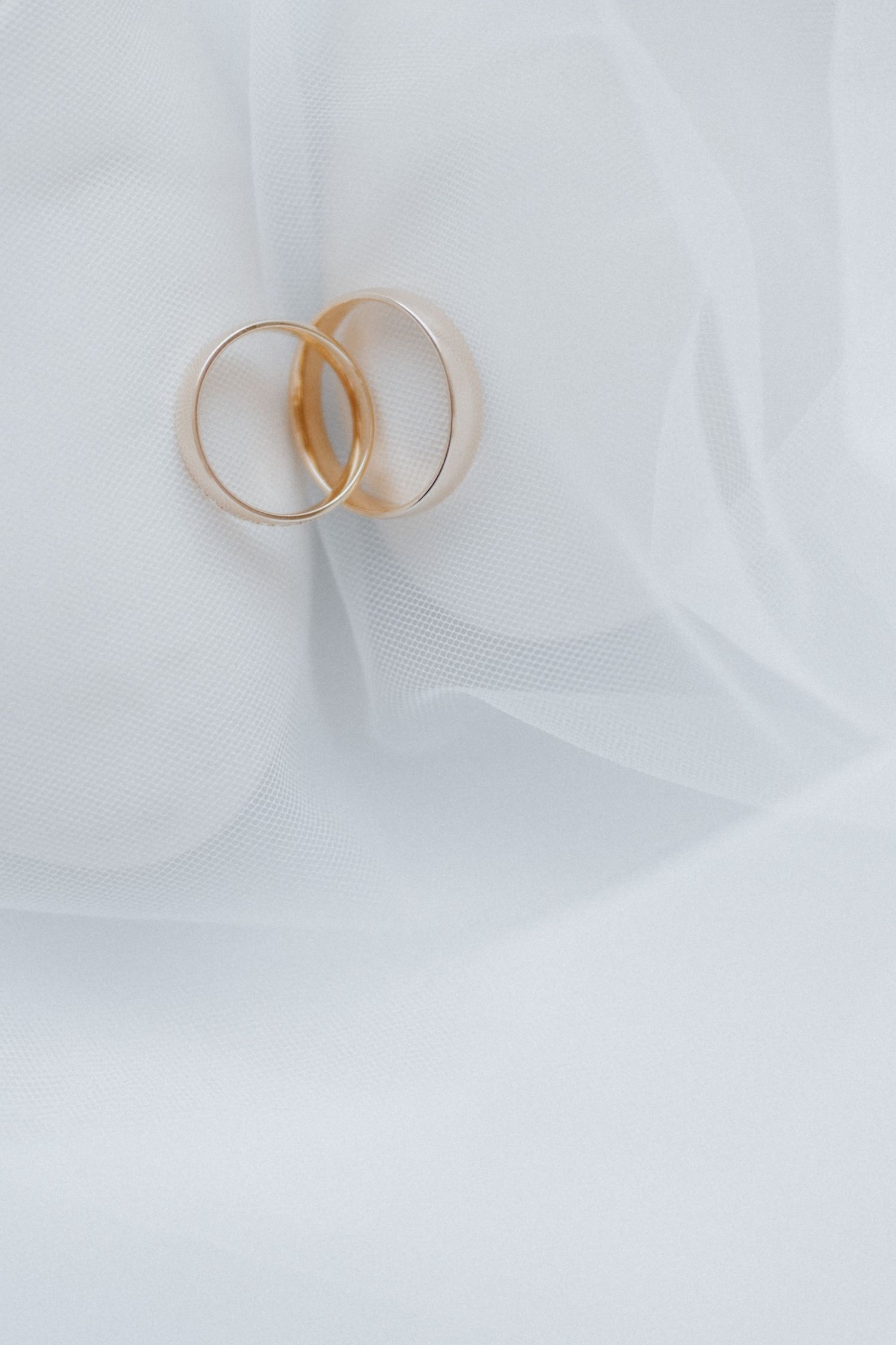 Two gold wedding rings resting on soft white bridal veil fabric, symbolizing marriage and eternal love.