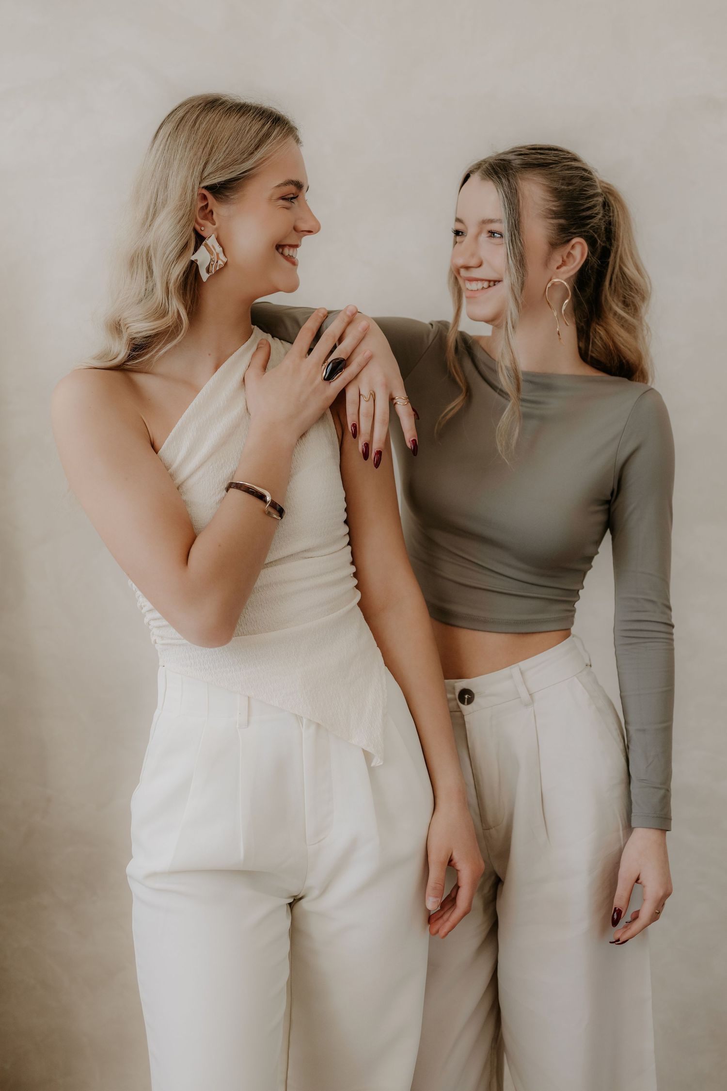 Two smiling blonde women in white pants and neutral tops laughing together in studio.