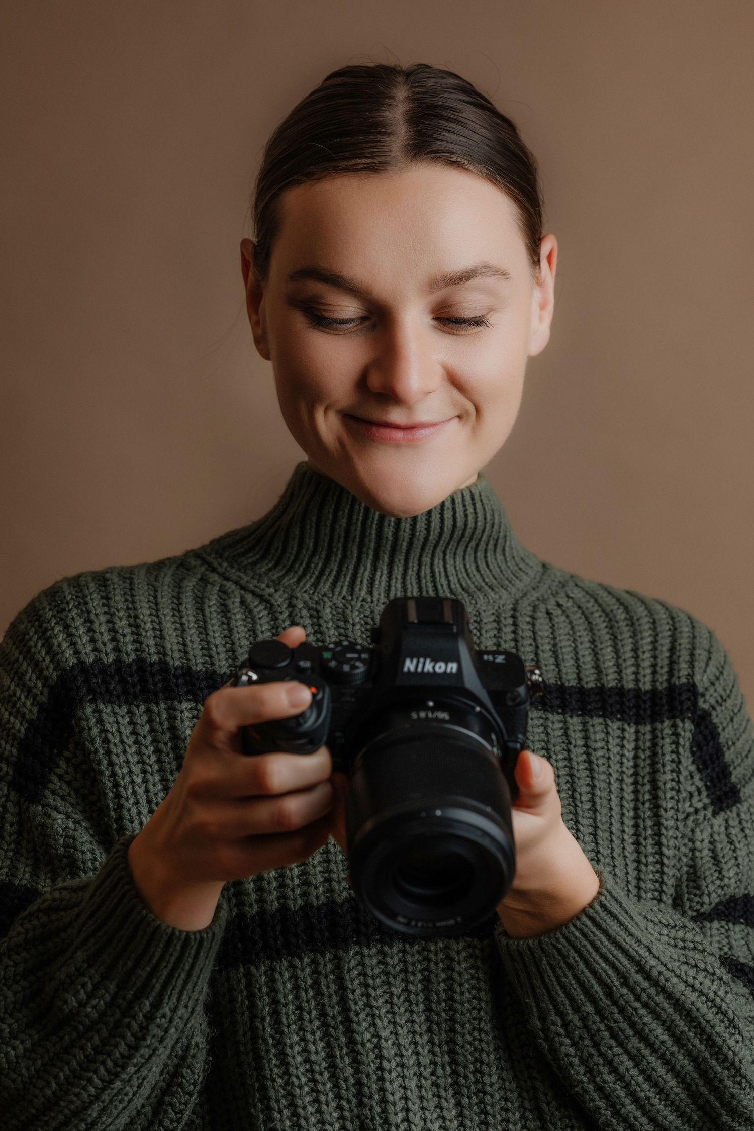 Young woman in green knit sweater smiling while reviewing photos on Nikon camera.